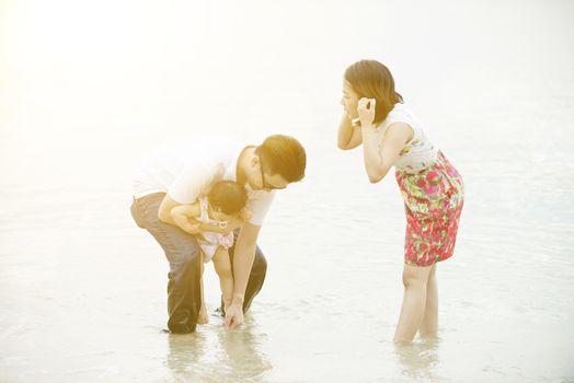 Happy Asian family outdoor activity together, having fun time at beach in sunset during vacations.