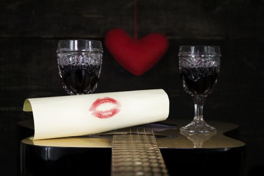 Happy Valentine's Day Kiss On White Paper Resting on Acoustic Guitar With Vine Glasses, Lights and Heart