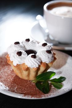 Cake on plate near cup of coffee on dark wooden table