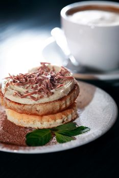 Cake on plate near cup of coffee on dark wooden table