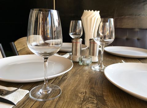 Restaurant interior. Set of empty wine glasses and plates on a dining table. Closeup of cutlery set for meal.