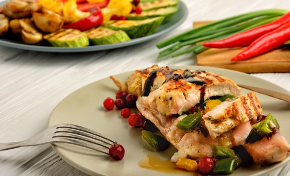 The juicy grilled chicken breast served on a plate and grilled vegetables on a white wooden background. Close up