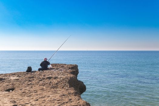old person fishing in the edge of the ocean on top of sedemenary rock