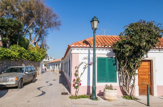 Beautiful typical rebuilt portuguese house in a village called cascais. with a pink frame in a sone made street surrounded by a garden and under the clear blue sky.
