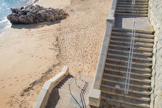 two flights of stairs to access a fine sand beach with a rock just at the edge of the water