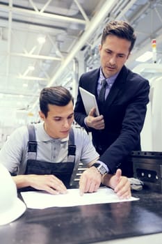 Manager and worker looking at technical documents at factory