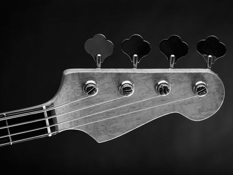 Black and white photo of a bass guitar headstock over dark background.