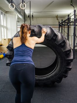 Photo of a young woman training in the gym with a tractor tire.
