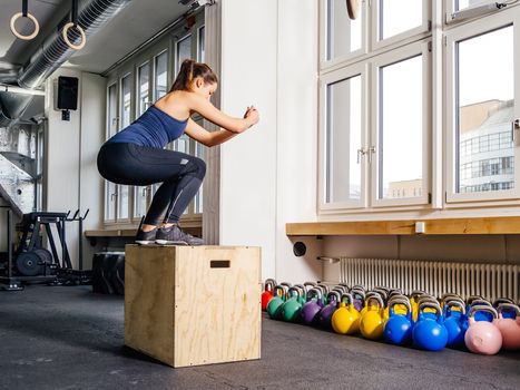 Photo of a young woman doing a box jump at the gym.