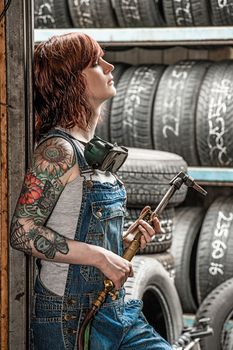 Photo of a beautiful redhead female mechanic with tattoos holding a welding torch.