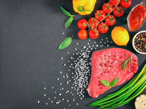 Raw meat. Raw beef steak on dark board with fresh herbs, vegetables, seasonings and spices. Top view or flat lay. Copy space