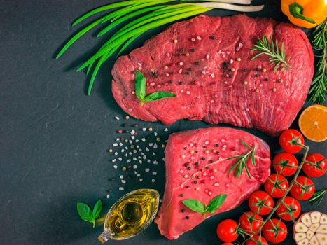 Raw meat. Raw beef steak on dark board with fresh herbs, vegetables, seasonings and spices. Top view or flat lay. Copy space