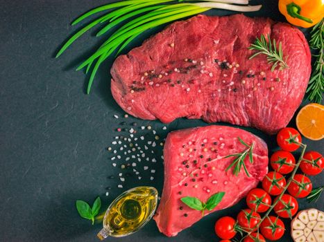 Raw meat. Raw beef steak on dark board with fresh herbs, vegetables, seasonings and spices. Top view or flat lay. Copy space