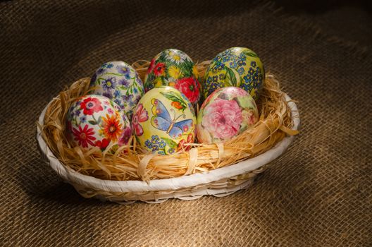 Decoupage Easter eggs are handmade in a wicker basket on burlap. Selective focus.