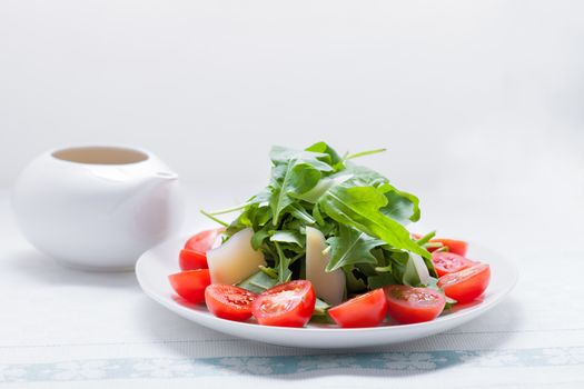 Salad with arugula, tomatoes served on a white plate