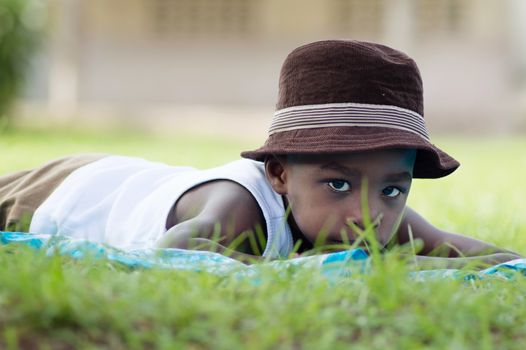 This child lying on a piece of cloth, looking at the camera, sits in the shade of a tree on the law.