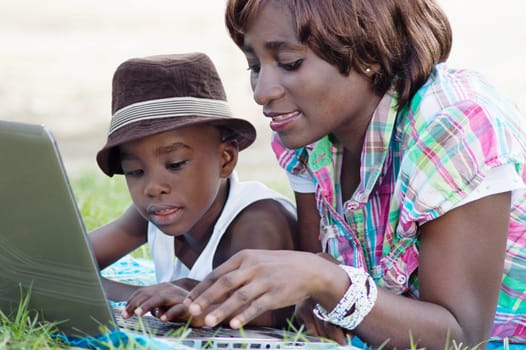 This woman and her son lying on the grass, working with his laptop.