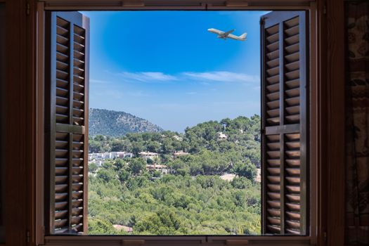 Landscape Houses and mountains seen through the window. In the background, blue sky and an airplane.