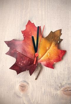 Autumn leaf with clock hands on top of a wooden background