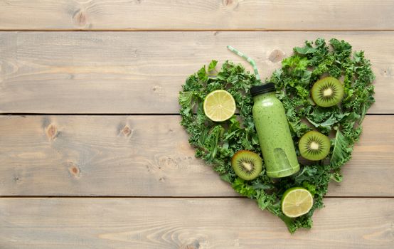 Bottled green smoothie with ingredients in a heart shape over a wooden table