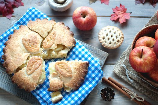 Sliced apple pie with fruit ingredients and cinammon sticks on one side 