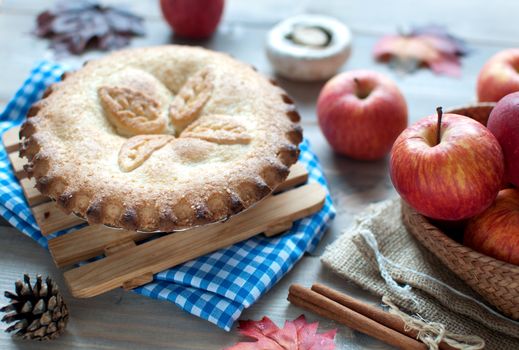 Apple pie with fruit ingredients autumn leaves and cinammon sticks on a wooden table