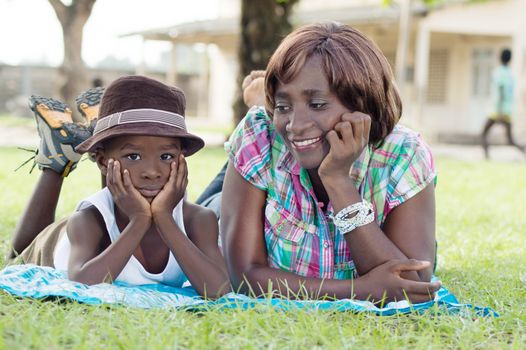 This young woman and her child are lying in the grass, mother smiling at her son.