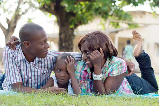 Young woman and her husband  smiled, and their child lying in the middle of them.