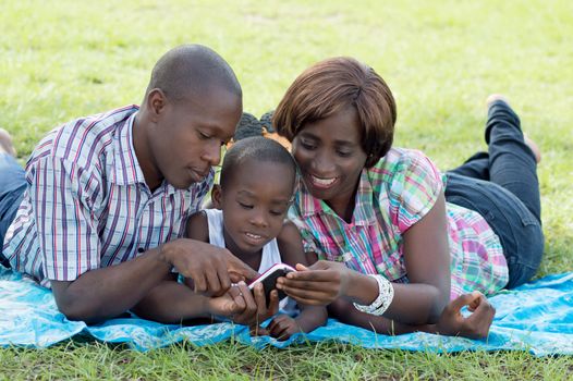 This  family lying on a piece of fabric in the grass, consult with their child a cell phone .