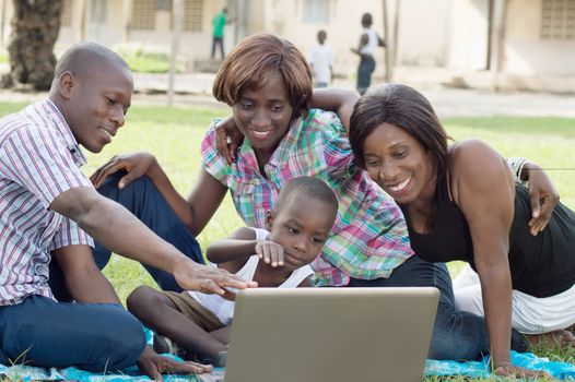 A group of friends and a child looking at a laptop screen . They are all happy.
