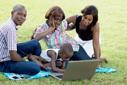 Women watch the child handle the laptop , while the man was staring at the camera.