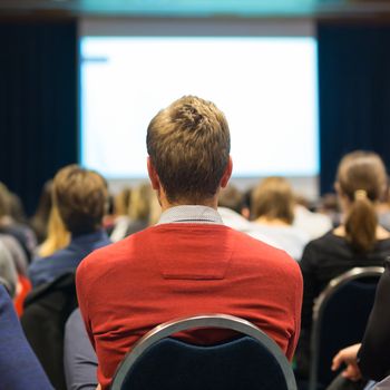 Business and entrepreneurship symposium. Speaker giving a talk at business meeting. Audience in the conference hall. Rear view of unrecognized participant in audience.