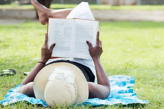 This young woman lying in the shade of a tree  is reading quietly.
