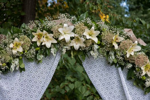 wedding arch decorated with white flowers lilies in a summer park
