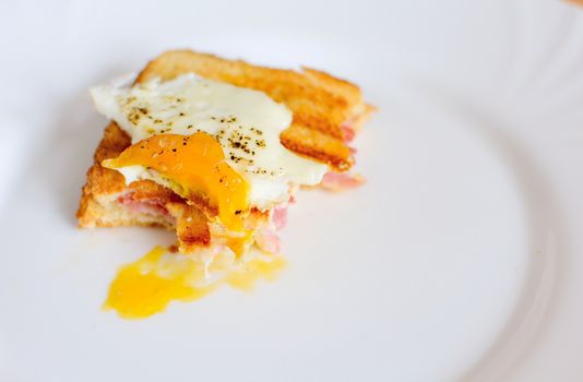 Leftover of ham and cheese toast with fried egg on top with missing bites.