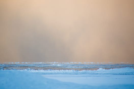 Sidelit snow squall clouds rolling in across the frozen Lake Huron at sunrise.  Ice floats on the still calm water.