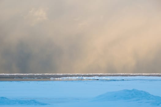 Sidelit snow squall clouds rolling in across the frozen Lake Huron at sunrise.  Ice floats on the still calm water.