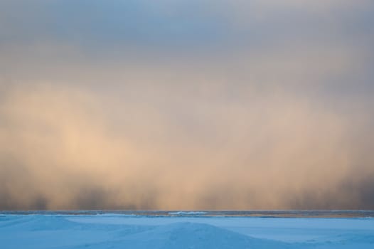 Sidelit snow squall clouds rolling in across the frozen Lake Huron at sunrise.  Ice floats on the still calm water.