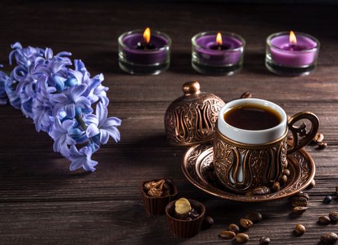 Cup of black coffee, candles and flowers on a wooden background. Dark key.