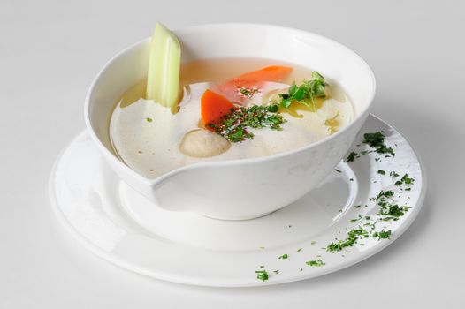 Clear soup with turkey meatballs, potatoes and other vegetables, served in white bowl