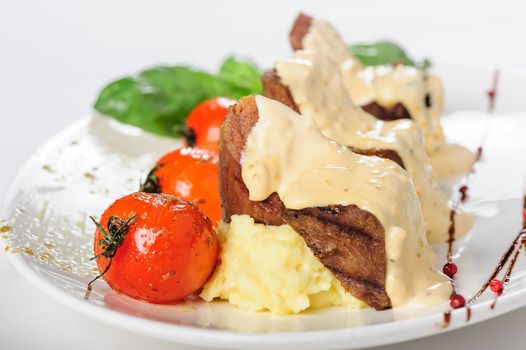 Baked mutton meat with creamy sauce, mashed potato and grilled cherry tomatoes, close up