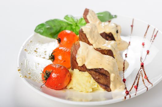 Baked mutton meat with creamy sauce, mashed potato and grilled cherry tomatoes, close up
