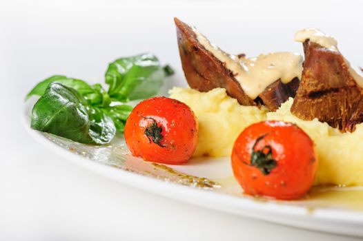 Baked mutton meat with creamy sauce, mashed potato and grilled cherry tomatoes, close up