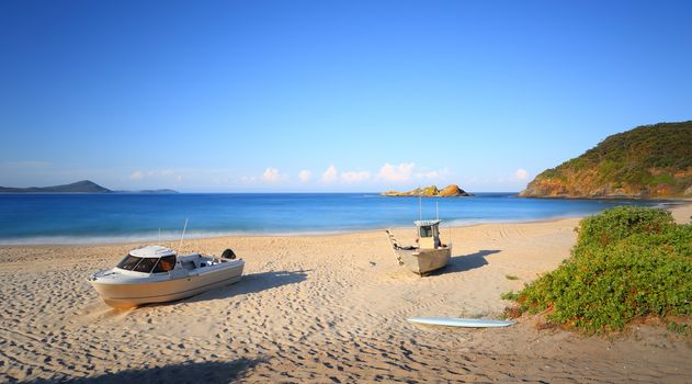 Two boats and a surfboard sit on Boat Beach, Seal Rocks Australia