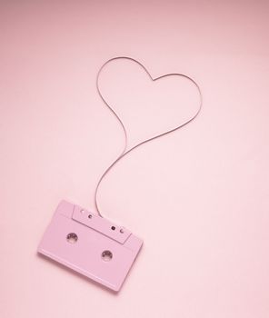 Creative love concept photo of painted cassette with tape in the shape of heart on pink  background.