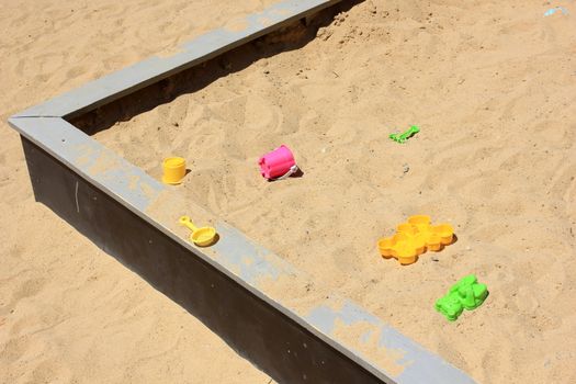 Children's sandbox with yellow sand and bright plastic toys