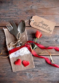 Valentines day label attached to cutlery inside a pouch with decorative ribbon and a single rose