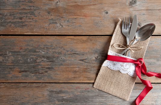 Rustic cutlery set with silk ribbon over a wooden background