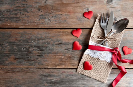 Cutlery set inside pouch with red hearts and silk ribbon over a wooden background