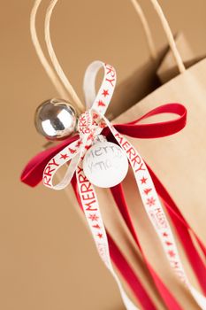 Close-up of Christmas gift bag of kraft paper with red and white ribbon decoration, vertical on brown background